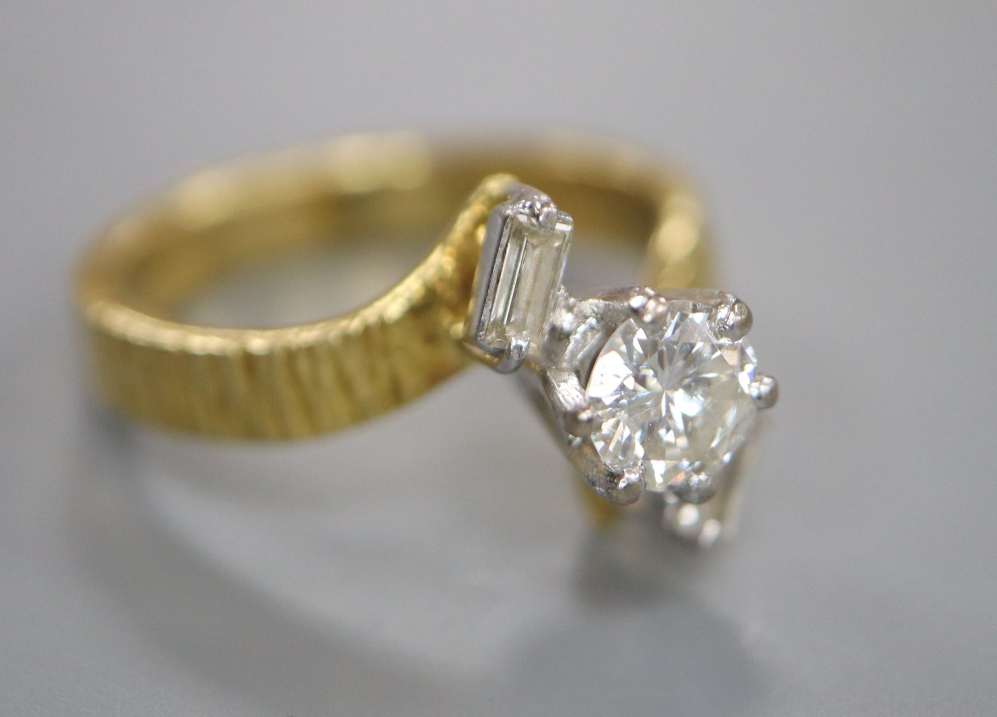 A modern textured 18ct gold and single stone diamond ring, with baguette cut diamond set shoulders,